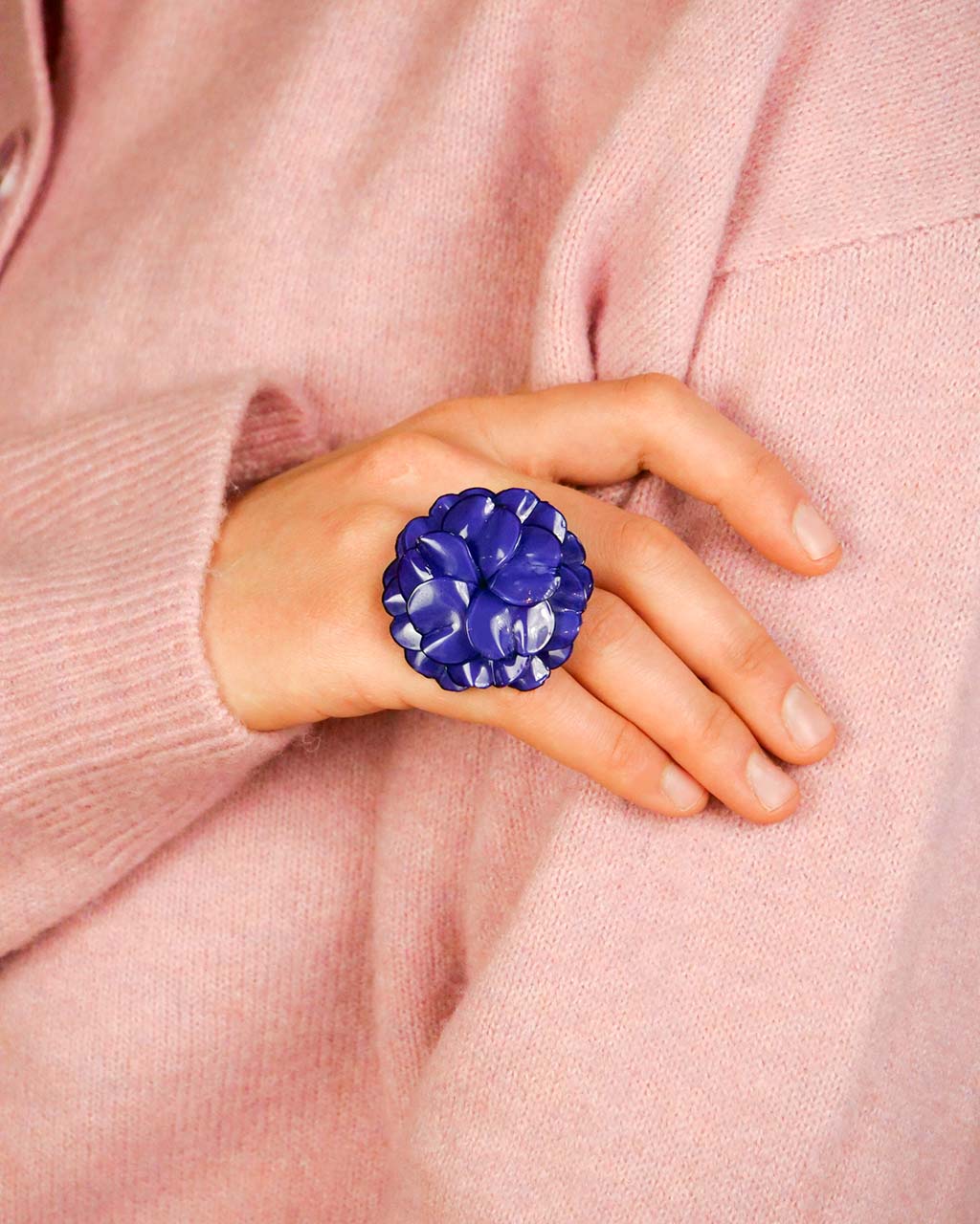 all-groups cette grande bague fleur géranium est portée par une jeune femme élégante avec un pull rose