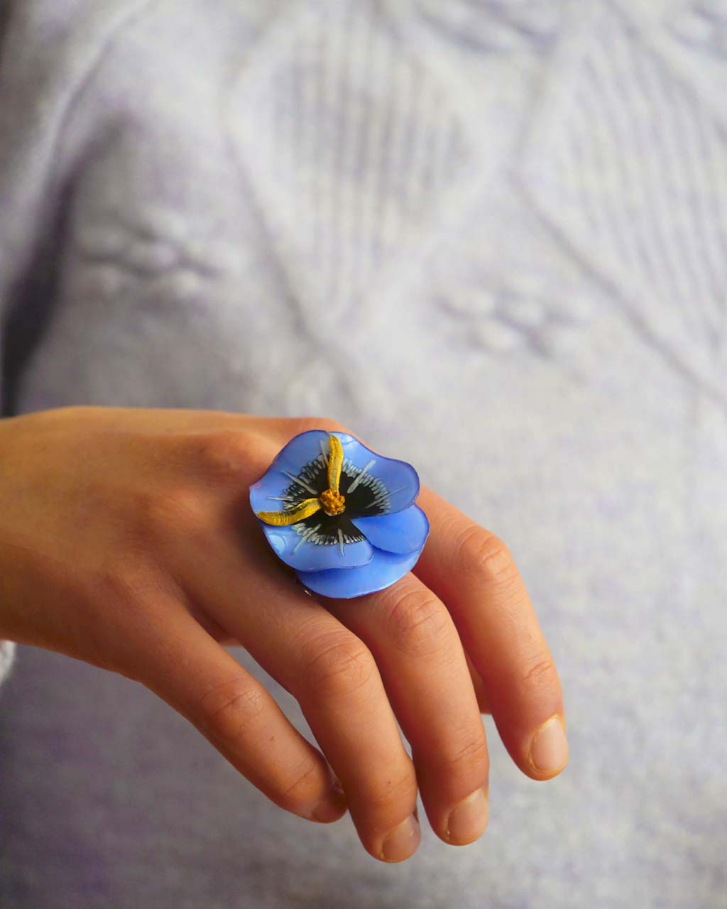 all-groups bague en résine bleue portée devant un pull lavande