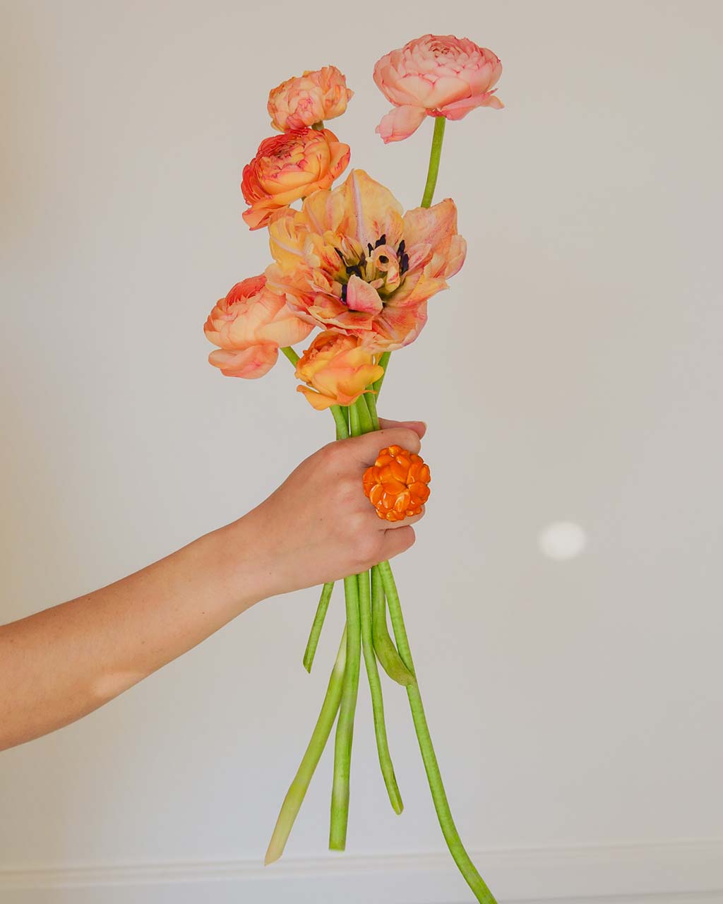 all-groups bague fleur orange sur une main tenant un bouquet de fleurs