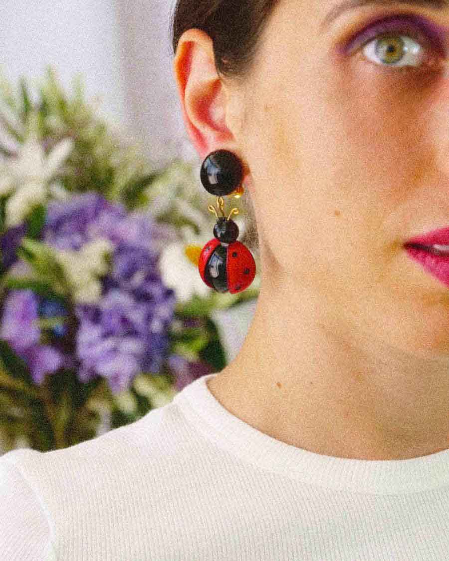 Femme portant des boucles d'oreilles coccinelles pendantes rouges et noires