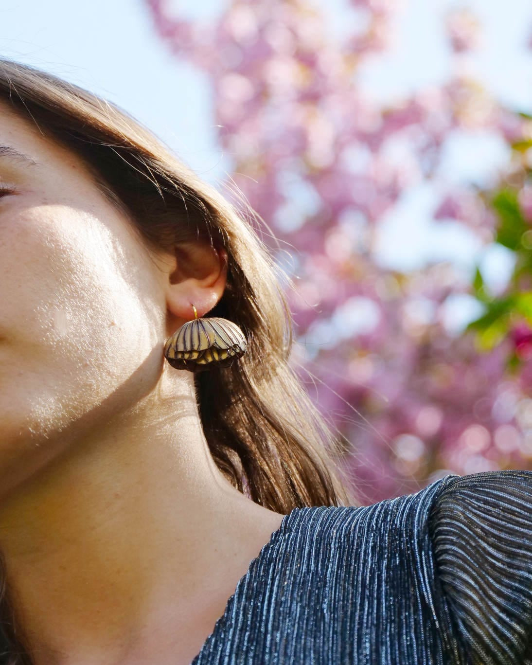 Les délicates boucles d'oreilles originales Destin, portées en extérieur par une jeune femme.
