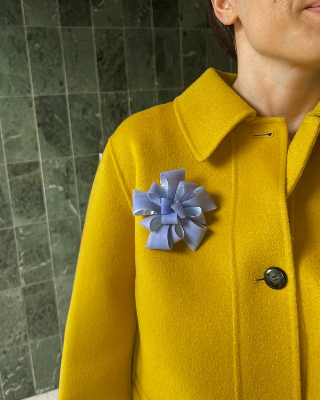 La broche bijoux Ambre bleu clair Ciléa Paris est portée par une jeune femme sur un manteau jaune pétant, créant un contraste lumineux.