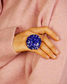 all-groups cette grande bague fleur géranium est portée par une jeune femme élégante avec un pull rose