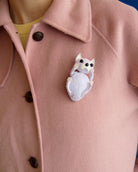 Ce bijou broche Billie représente un chien blanc porté sur un manteau rose.