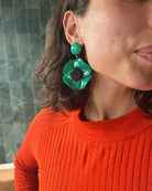 all-groups femme portant un pull orange et des boucles d'oreilles vertes en forme de fleur