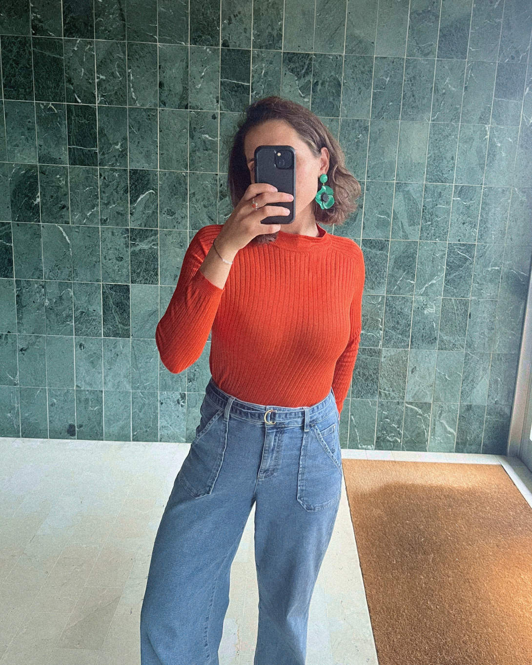 all-groups femme portant un pull orange et des boucles d'oreilles vertes fleurs