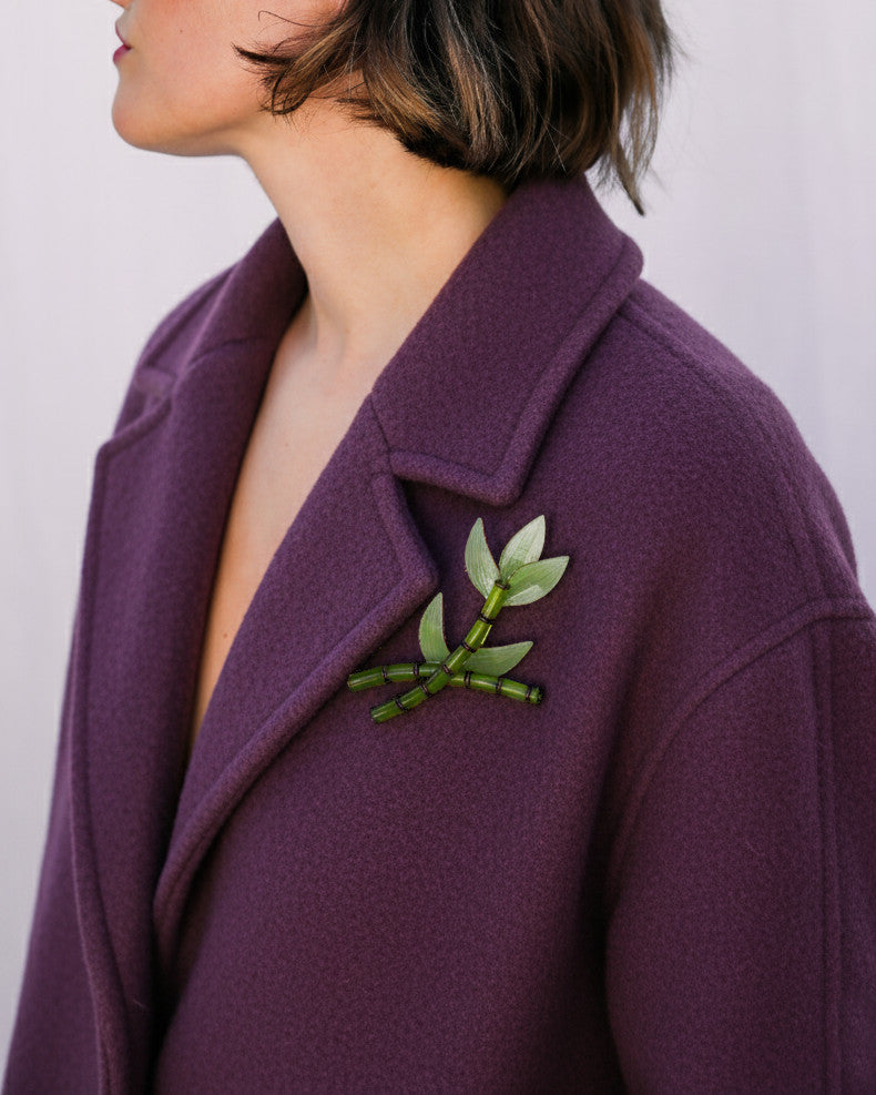all-groups femme portant un manteau violet sur lequel elle a mis une broche n forme de bambou