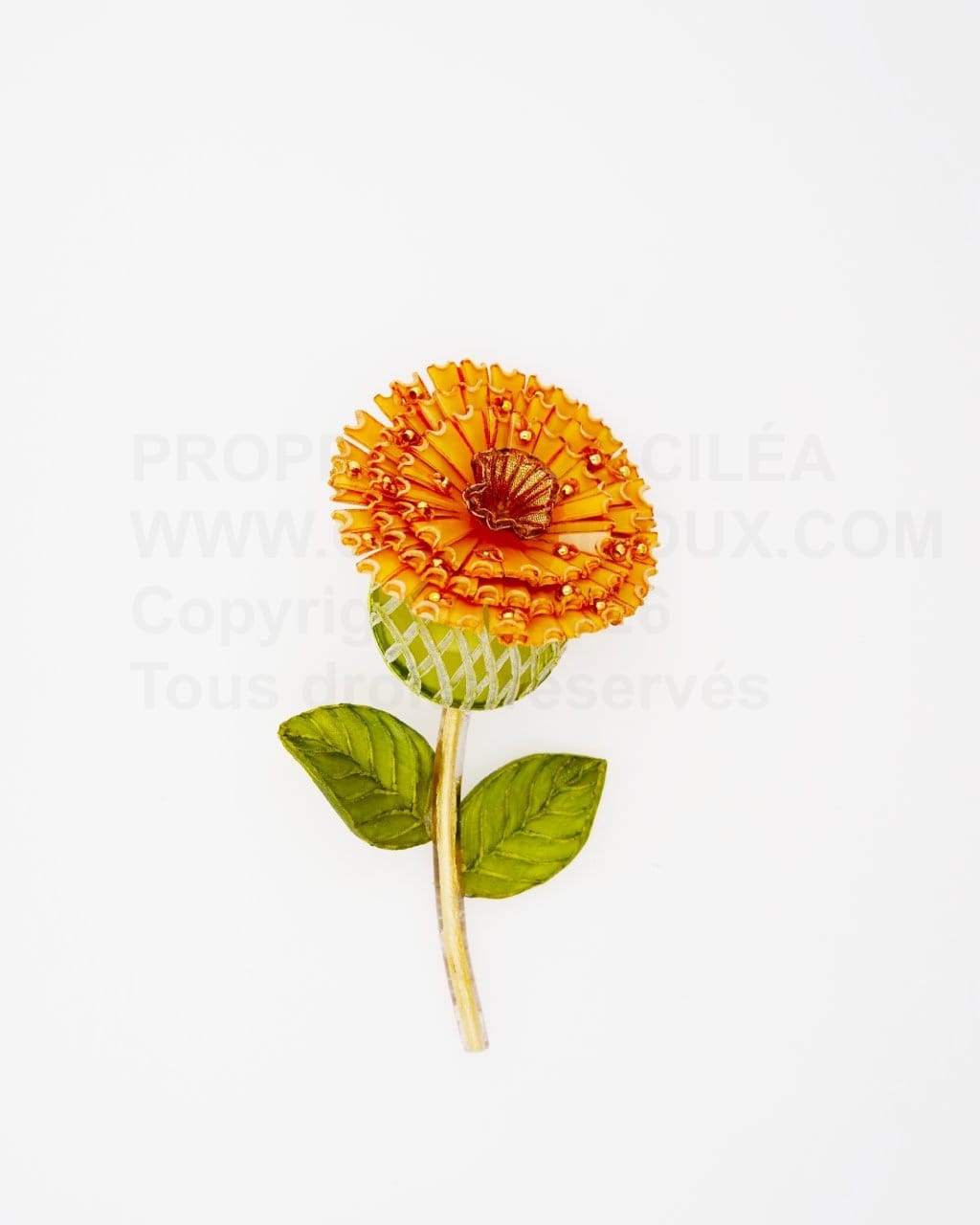 Broche Blume composée d'une grande fleur orange accompagnée de sa tige dorée et de ses feuilles vertes.