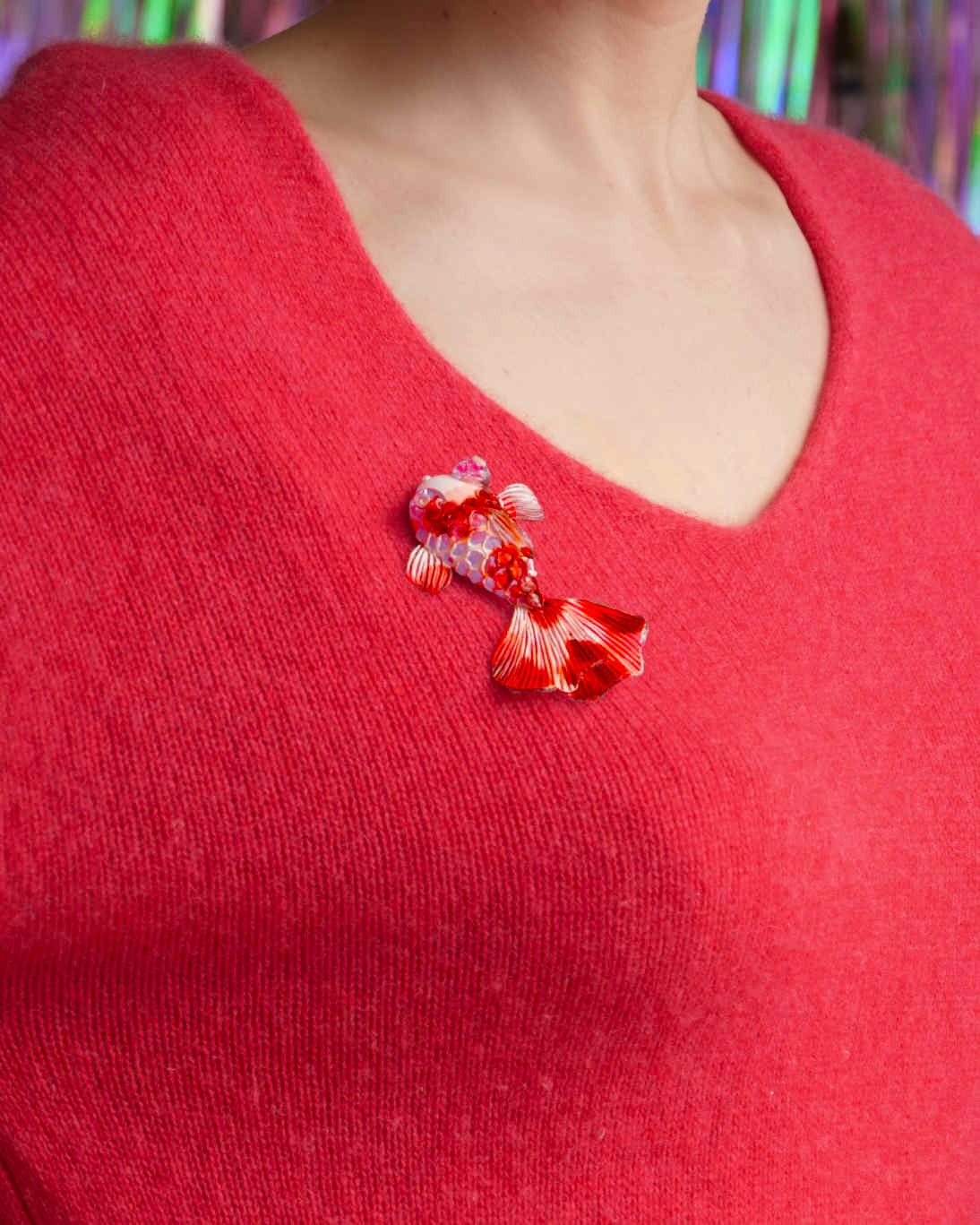 all-groups femme avec un pull rouge portant une broche bijou poisson