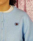 all-groups pins fleur Pensée bleu portée par une femme avec un pull bleu océan